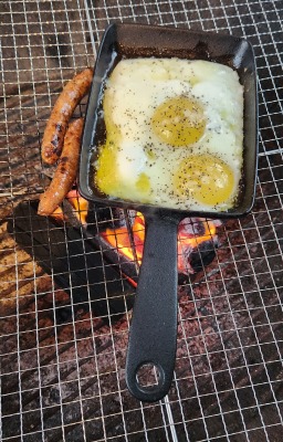 炭で焼いている目玉焼きとソーセージ