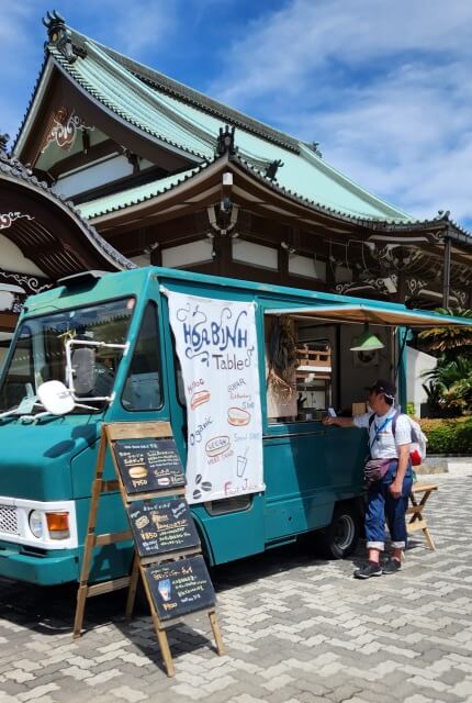 お寺をバックにしたホアビンテーブルのブルーのキッチンカー。